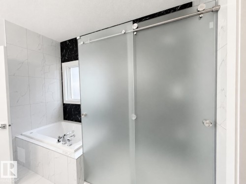 Frosted glass sliding shower door with stainless steel hardware, set against a backdrop of white and black veined tiling - 415 42 Street, Edmonton, AB 