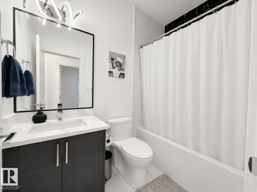Modern bathroom featuring a dark grey vanity with a white countertop, an integrated rectangular sink, and a framed mirror - 415 42 Street, Edmonton, AB 