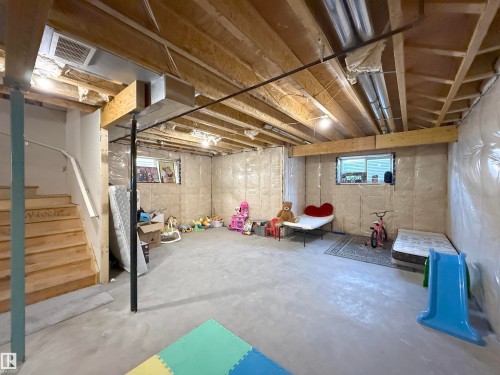 Unfinished lower level featuring exposed wood joists, concrete flooring, insulated walls, and a visible staircase with a white railing - 415 42 Street, Edmonton, AB 