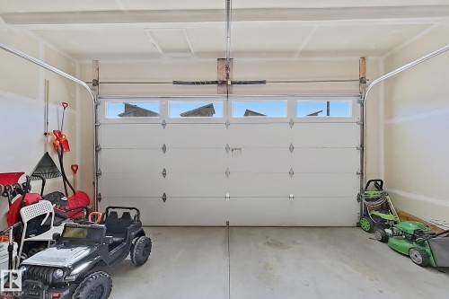 Spacious garage featuring a paneled garage door with upper window inserts, an automatic garage door opener system, unfinished walls, and a concrete floor - 415 42 Street, Edmonton, AB 