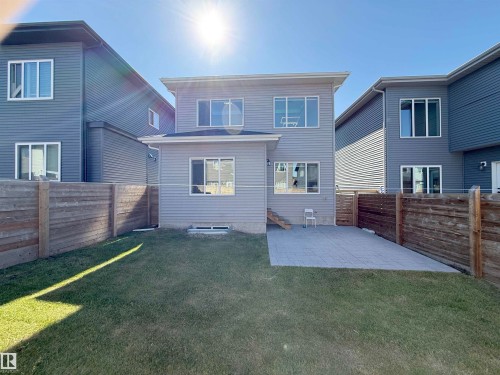 Exterior featuring light gray siding with white trim, multiple windows, a rear patio with paver stones, a grass lawn, and wood privacy fencing - 415 42 Street, Edmonton, AB 