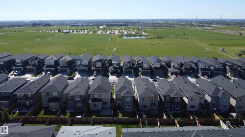 Aerial perspective showcasing a collection of modern residential properties with dark shingle roofs, individual private yards, and direct access to a large green field with a distant pond - 415 42 Street, Edmonton, AB 