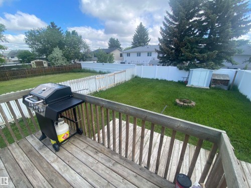 Expansive backyard featuring a wood deck, green lawn, white privacy fencing, a white storage shed, and a stone-lined fire pit - 5713 44A Street, Vegreville, AB 