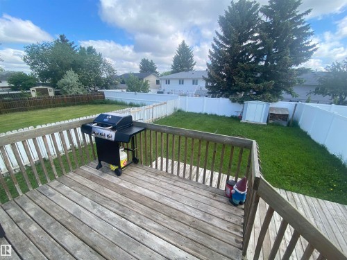 Wood-plank deck with a perimeter railing, overlooking a green lawn with a white privacy fence and a storage shed - 5713 44A Street, Vegreville, AB 