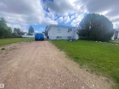 Single-story residence with a gravel driveway, expansive front lawn, mature front-yard tree, and a light-colored exterior - 5713 44A Street, Vegreville, AB 