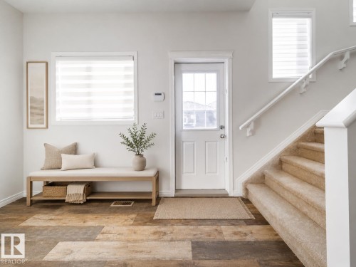 Entryway featuring multi-tone wood-finish flooring, a white paneled door with glass insert, and a carpeted staircase with white railings - 1199 Watt Drive, Edmonton, AB 