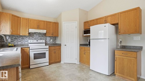 Kitchen featuring wood-finish cabinetry, a patterned tile backsplash, and light-toned tile flooring - 6105 52 Avenue, Beaumont, AB 