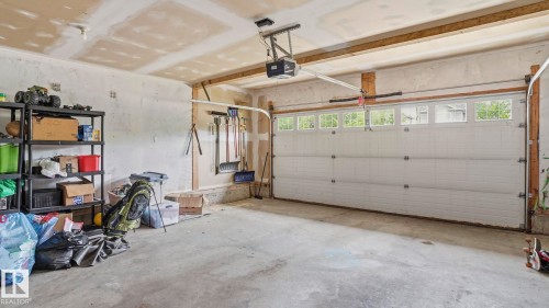 Attached garage featuring a concrete floor, exposed ceiling joists, and a white paneled garage door with upper window inserts and an automatic opener - 6105 52 Avenue, Beaumont, AB 