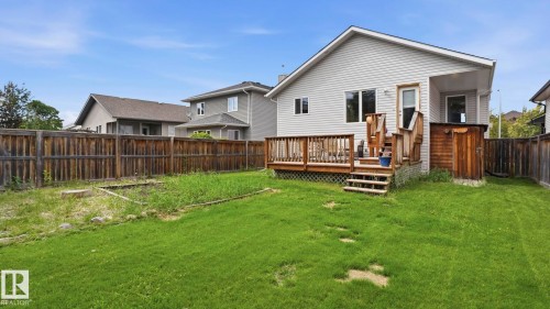 Rear exterior featuring a wood-plank deck, wood-plank privacy fence, and an expansive lawn - 6105 52 Avenue, Beaumont, AB 
