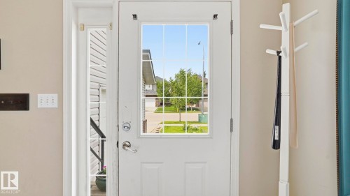 White paneled entry door with grid-patterned glass insert and brushed nickel hardware, accompanied by a full-length sidelight with integrated grids - 6105 52 Avenue, Beaumont, AB 
