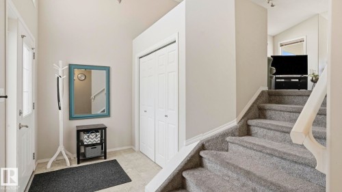 Tiled entryway featuring a front door with glass panels, a double-door closet, and a carpeted staircase with a white wooden railing - 6105 52 Avenue, Beaumont, AB 