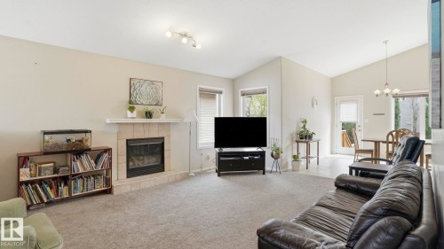 Spacious living area featuring a fireplace with a light-toned tile surround and mantel, vaulted ceilings, track lighting, and a glass-paneled exterior door - 6105 52 Avenue, Beaumont, AB 