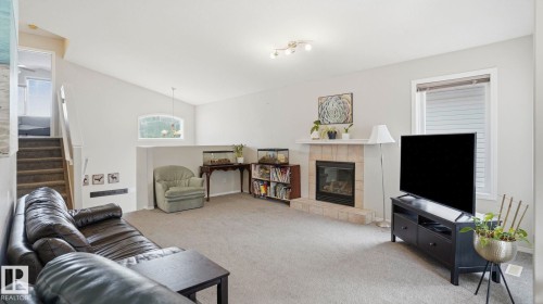 Living area featuring a tile-surround fireplace with a white mantel, light gray carpeting, and a window with blinds - 6105 52 Avenue, Beaumont, AB 
