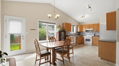Vaulted ceilings highlight this kitchen and dining area with wood cabinetry, tile flooring, and white appliances - 6105 52 Avenue, Beaumont, AB 