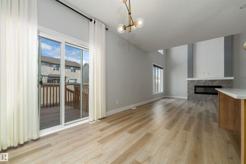 Open-concept living area featuring light wood-finish flooring, a modern fireplace with a tiled hearth and shiplap-style surround, and a two-story ceiling - 17320 9 Avenue, Edmonton, AB 