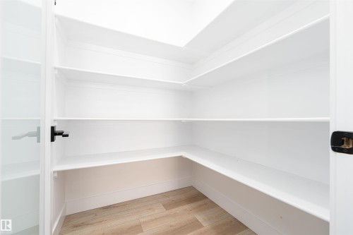 Walk-in pantry featuring extensive white shelving, wood-finish flooring, and a modern black door handle - 17320 9 Avenue, Edmonton, AB 