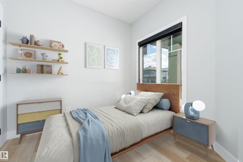 Light-filled bedroom featuring wood-finish flooring, white walls, a large window with a dark roller shade, and three wall-mounted floating shelves - 17320 9 Avenue, Edmonton, AB 