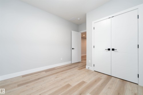 Spacious room featuring light wood-finish flooring, crisp white walls, and contemporary white doors with matte black hardware - 17320 9 Avenue, Edmonton, AB 