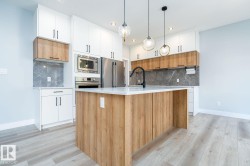 Contemporary kitchen featuring a large central island with a white countertop, wood-finish base, and pendant lighting - 