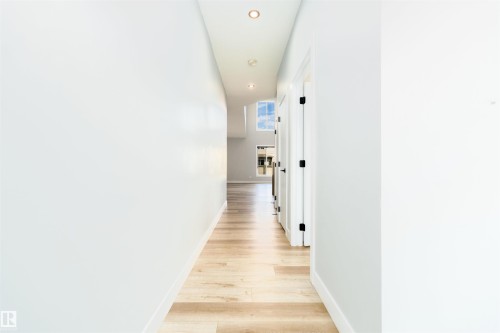 Hallway featuring wood-finish flooring, recessed lighting, white walls, and multiple white doors with dark hardware - 17320 9 Avenue, Edmonton, AB 
