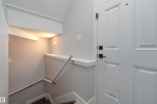 Stairwell with light gray wall paint and white trim, featuring a contemporary white panel door with matte black hardware, recessed ceiling lighting, and a built-in wall niche with accent lighting - 17320 9 Avenue, Edmonton, AB 