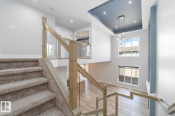 Open concept interior featuring a two-story ceiling, multiple windows, a modern chandelier, light wood-finish flooring, and a staircase with glass panel railing - 