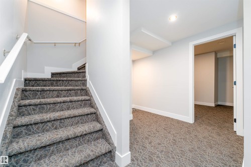 Carpeted staircase featuring a white handrail, leading to a hallway with patterned carpeting, recessed lighting, and a white baseboard - 17320 9 Avenue, Edmonton, AB 