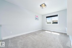 Spacious room featuring light gray carpeting, a large window with a dark roller shade, a modern flush-mount light fixture, white baseboards, and light-colored walls - 
