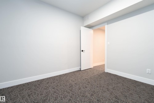 Minimalist room featuring light gray walls, white trim, and patterned gray carpeting - 17320 9 Avenue, Edmonton, AB 
