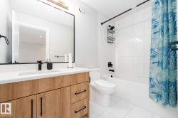 Bathroom featuring a wood-finish vanity with a white countertop and integrated sink, complemented by a matte black faucet - 