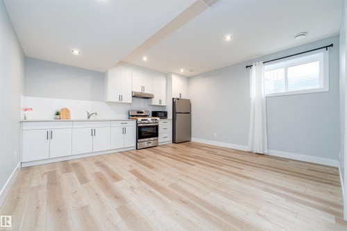 Open-concept living space with light wood-finish flooring, white cabinetry, recessed lighting, and stainless steel appliances - 17320 9 Avenue, Edmonton, AB 