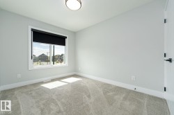 Room with light grey wall paint, plush grey carpet, a white framed window with black roller shade, and a white interior door with matte black hardware - 