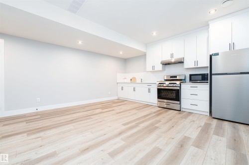 Contemporary kitchen area featuring stainless steel appliances, white cabinetry, recessed lighting, and wood-finish flooring - 17320 9 Avenue, Edmonton, AB 