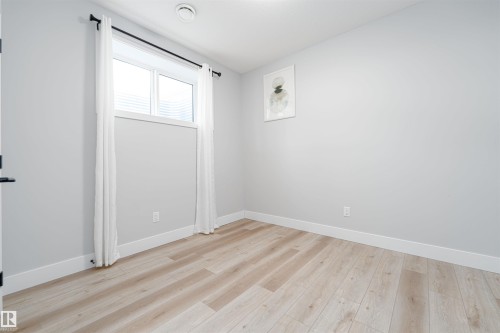 Bright room with light wood-finish flooring, white baseboards, and a window with white trim - 17320 9 Avenue, Edmonton, AB 