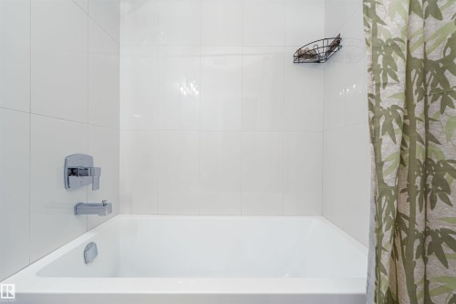 White bathtub with polished chrome fixtures and white tiled surround - 17320 9 Avenue, Edmonton, AB 