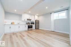 Modern kitchen area featuring white cabinetry, stainless steel appliances, and a light wood-finish flooring - 