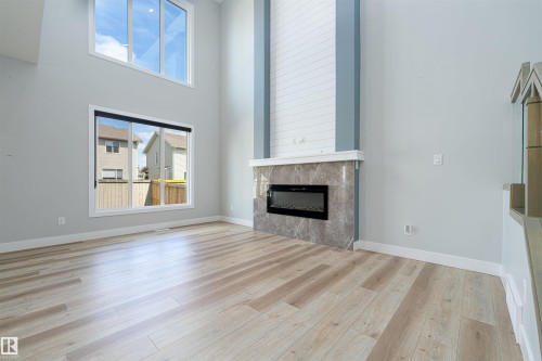Living area featuring high ceilings with upper transom windows, light wood-finish flooring, and a contemporary linear electric fireplace with a stone-finish surround and shiplap accent wall - 17320 9 Avenue, Edmonton, AB 