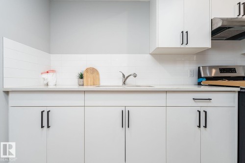 Bathroom featuring a light wood-finish floor, a white vanity with an integrated sink, a white countertop, and a large black-framed mirror - Edmonton, AB 