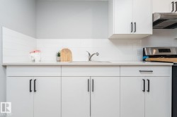Modern kitchen featuring white cabinetry, light-toned countertops, a stainless steel sink with a chrome faucet, white subway tile backsplash, and stainless steel appliances - 