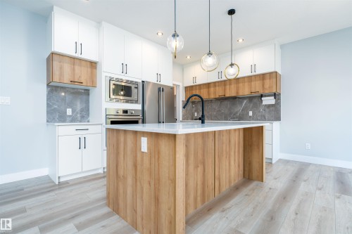 Modern kitchen featuring a central island with wood-finish paneling and a light-toned countertop - 17320 9 Avenue, Edmonton, AB 