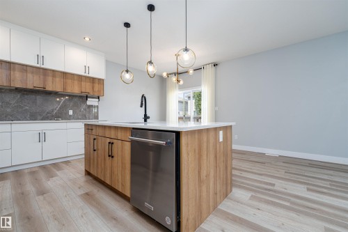 Kitchen featuring a central island with a built-in sink and stainless steel dishwasher - 17320 9 Avenue, Edmonton, AB 