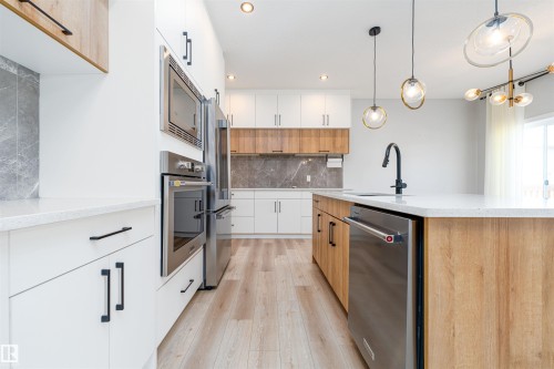 Modern kitchen featuring a central island with a built-in sink and stainless steel dishwasher - 17320 9 Avenue, Edmonton, AB 