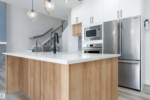 Kitchen island featuring a light wood-finish base, white countertop, and matte black faucet - 17320 9 Avenue, Edmonton, AB 