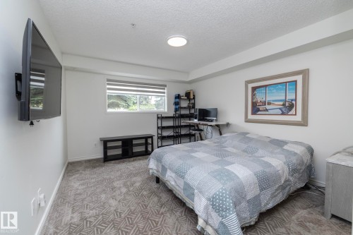 Carpeted room featuring a window with horizontal blinds, a wall-mounted flat-screen television, a built-in floating desk, and recessed ceiling lighting - 111 182 Haddow Close, Edmonton, AB 