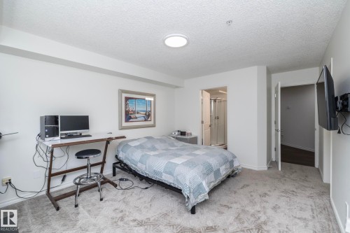 Carpeted room featuring a ceiling-mounted light fixture, white walls, and a doorway revealing a bathroom with a glass shower enclosure - 111 182 Haddow Close, Edmonton, AB 