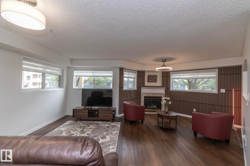 Living area featuring wood-finish flooring, a corner fireplace with a white mantel, and multiple windows - 111 182 Haddow Close, Edmonton, AB 