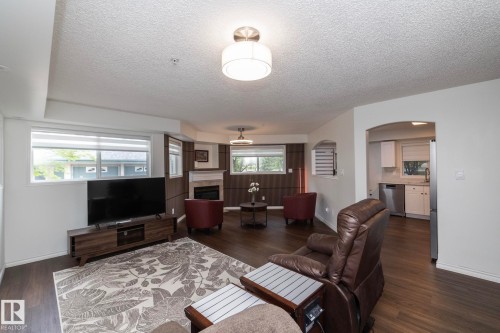 Spacious living area featuring wood-finish flooring and a decorative fireplace with a white mantel - 111 182 Haddow Close, Edmonton, AB 