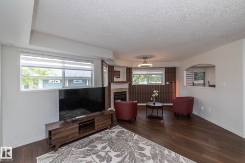 Spacious interior featuring wood-finish flooring, a contemporary fireplace with a light-toned mantel, and a recessed archway - 111 182 Haddow Close, Edmonton, AB 