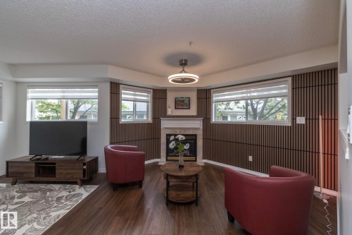 Living area featuring wood-finish flooring, multiple windows with blinds, a built-in fireplace with a mantel, and decorative wall paneling - 111 182 Haddow Close, Edmonton, AB 