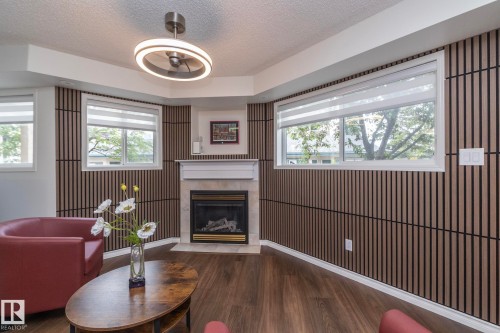 Living area featuring a gas fireplace with a white mantel, wood-finish flooring, and slatted accent walls - 111 182 Haddow Close, Edmonton, AB 